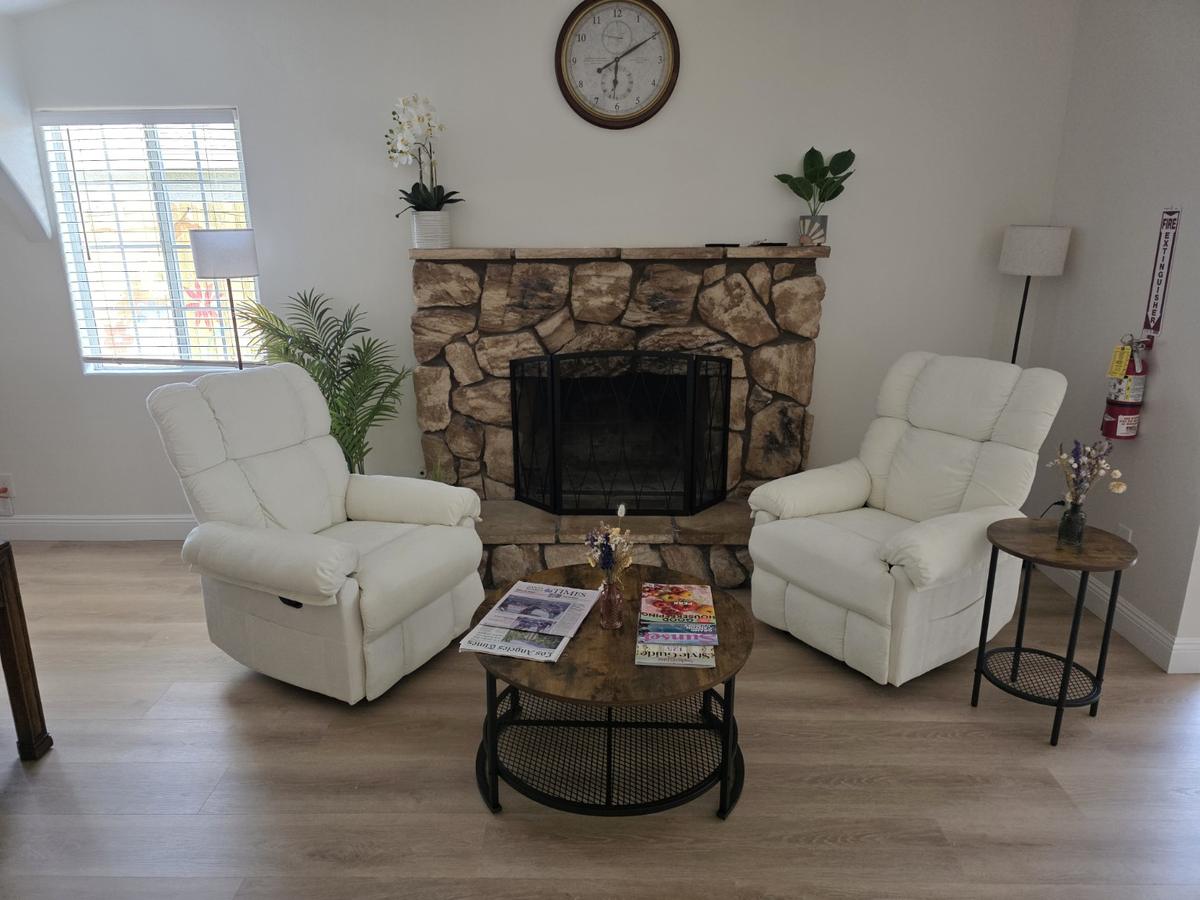 Two white recliners facing the stone fireplace with a coffee table and newspapers