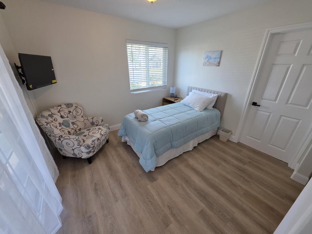 Private bedroom with a made bed, upholstered chair, wall-mounted television and window